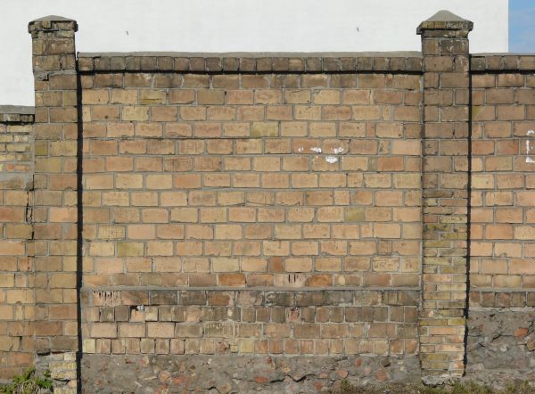 Brick fence texture made up of bricks in various shades of tan and brown, with a strip of grey cement with brick fragments near the bottom.